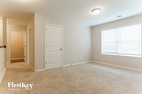 A spacious room with a carpeted floor and a window with blinds.