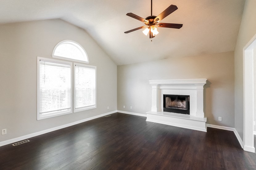 an empty living room with a fireplace and a ceiling fan