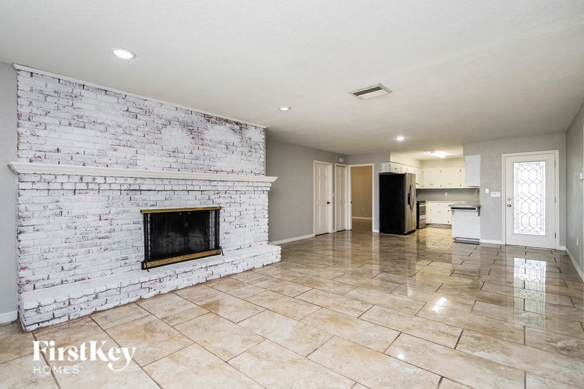 an empty living room with a white brick fireplace and tiled floors