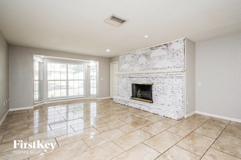 an empty living room with a brick fireplace and tiled floors