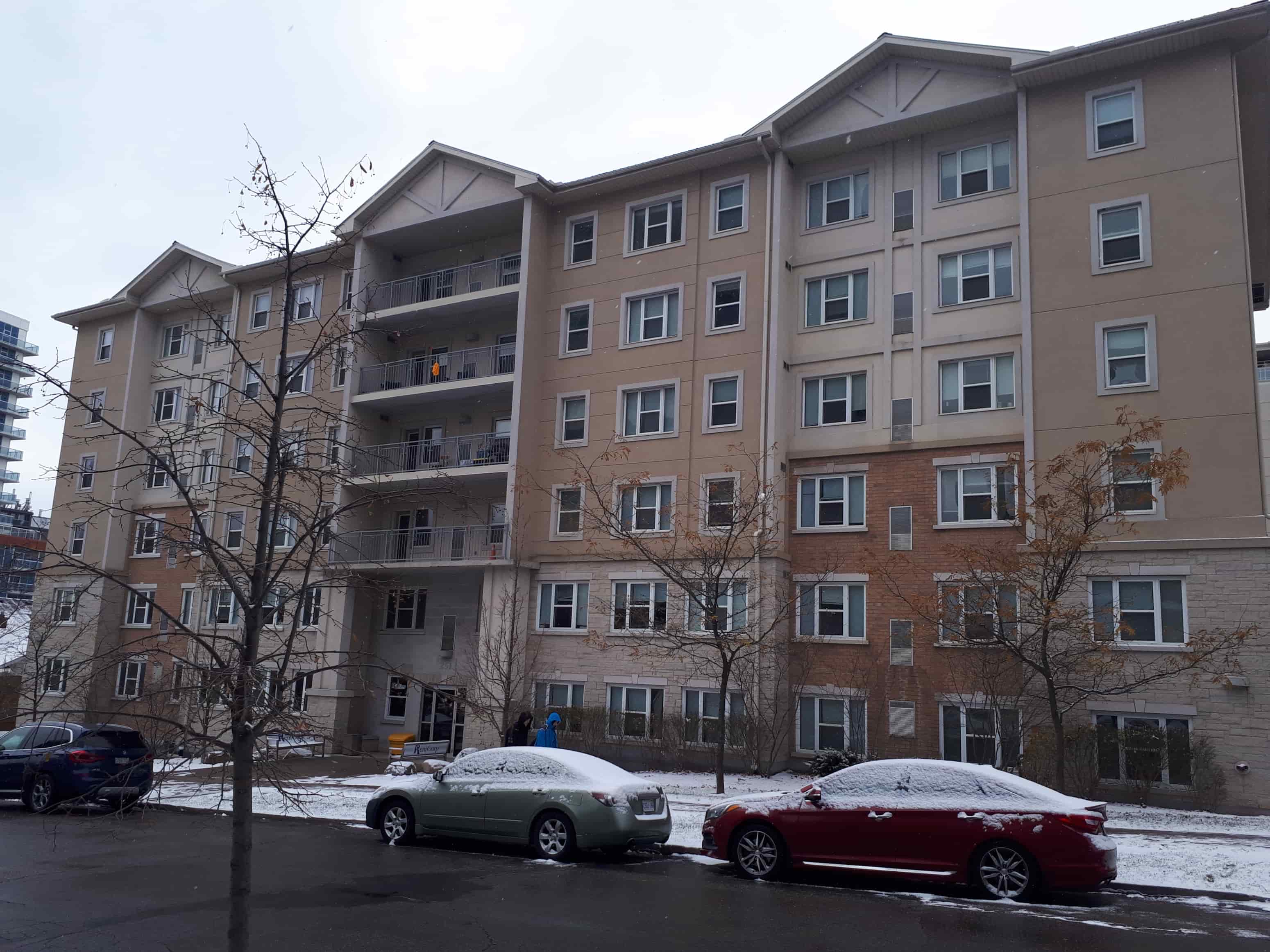 Two cars are parked in a parking lot in front of a large apartment building.