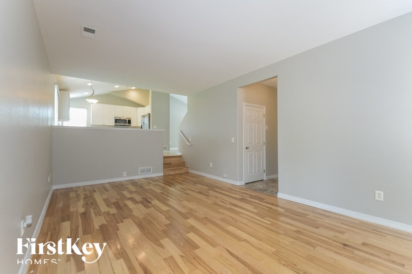 an empty living room with wood flooring and a kitchen