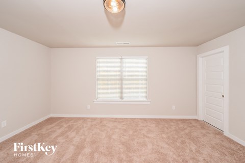 A room with a carpeted floor, a window with blinds, and a door.