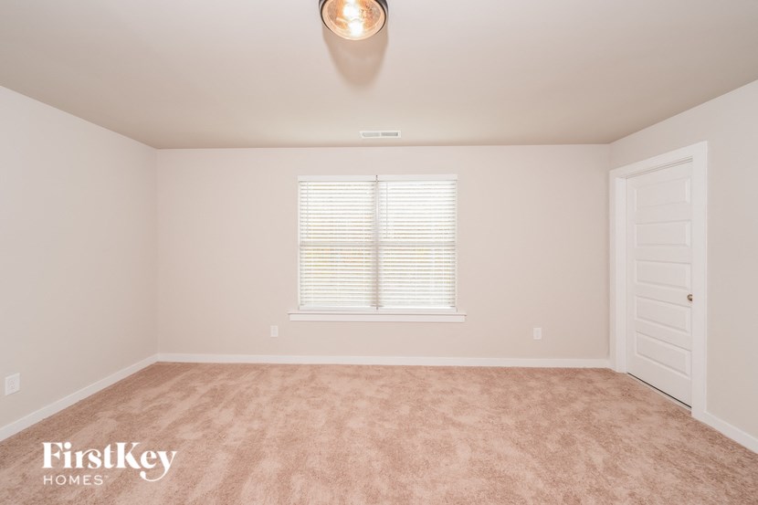 A room with a carpeted floor, a window with blinds, and a door.