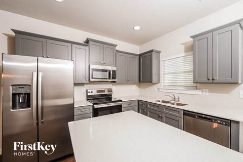 A kitchen with a refrigerator, microwave, oven, and sink.