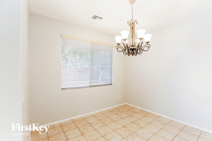 A room with a chandelier, tiled floor, and a window with blinds.