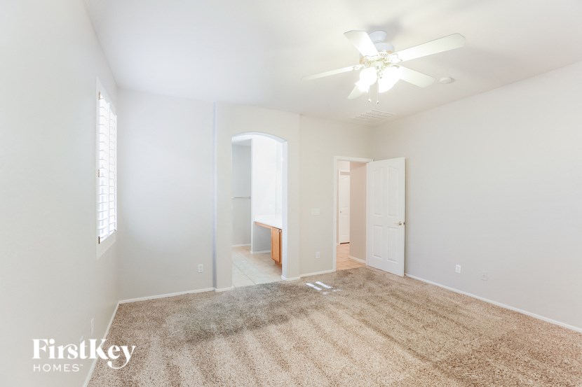 A carpeted room with a ceiling fan and three doors.