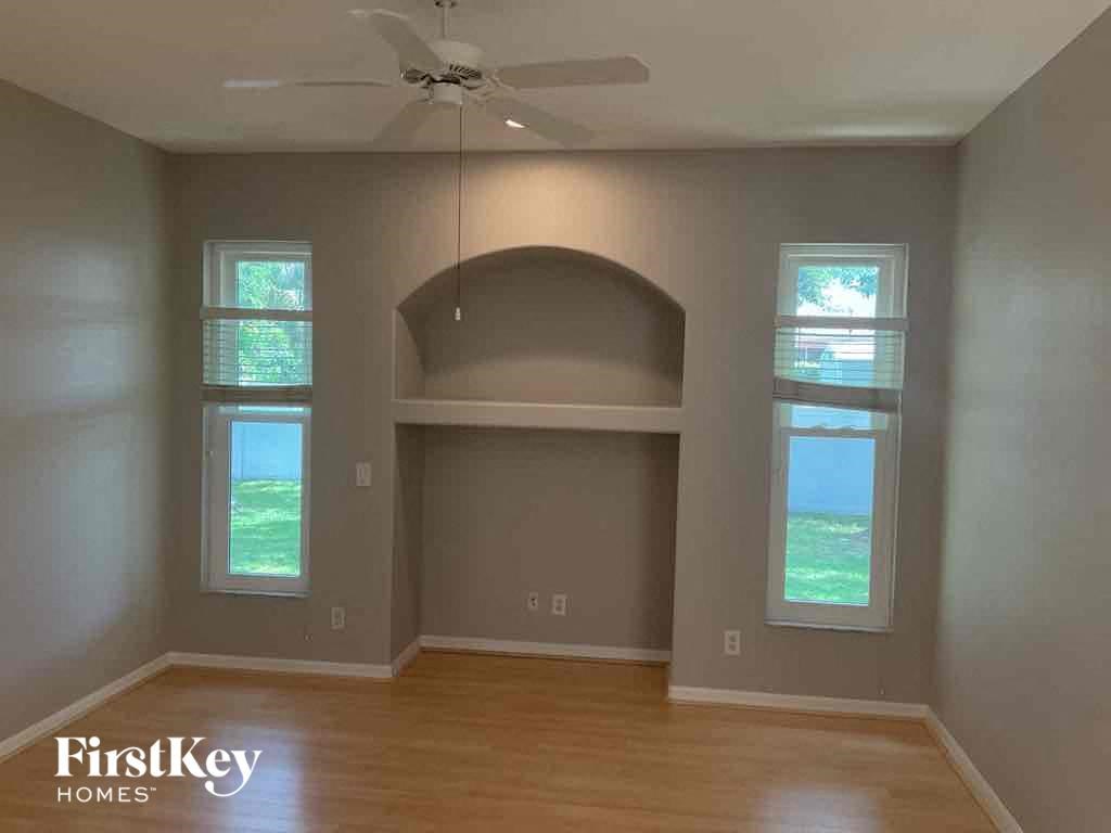 A room with a fan and a window with a view of the grass.