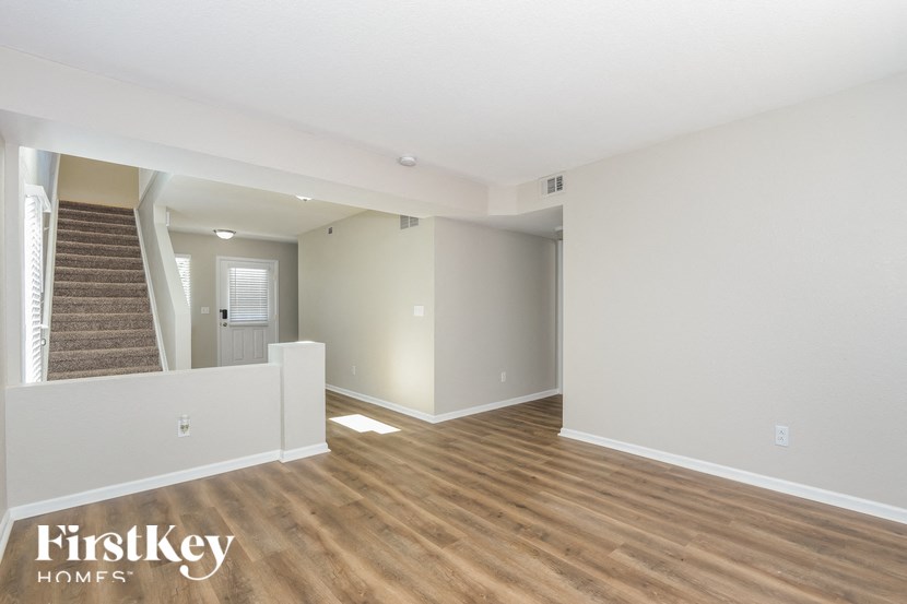A spacious room with wooden flooring and a staircase leading to another room.