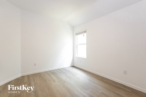 a bedroom with white walls and wood floors and a window