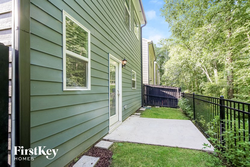 the walkway to the front door of a green house with a black fence