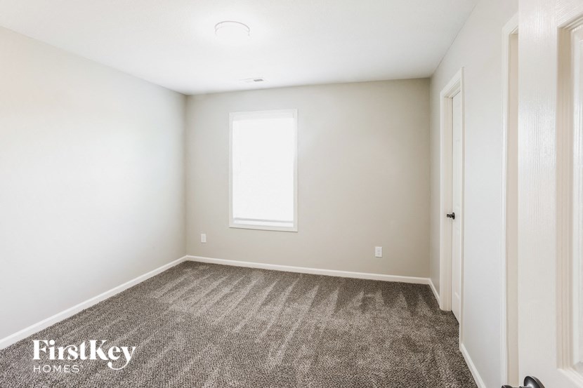 A carpeted room with a window and a door.