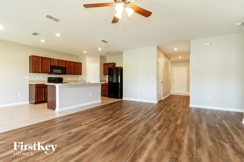 an empty living room with a kitchen and a ceiling fan