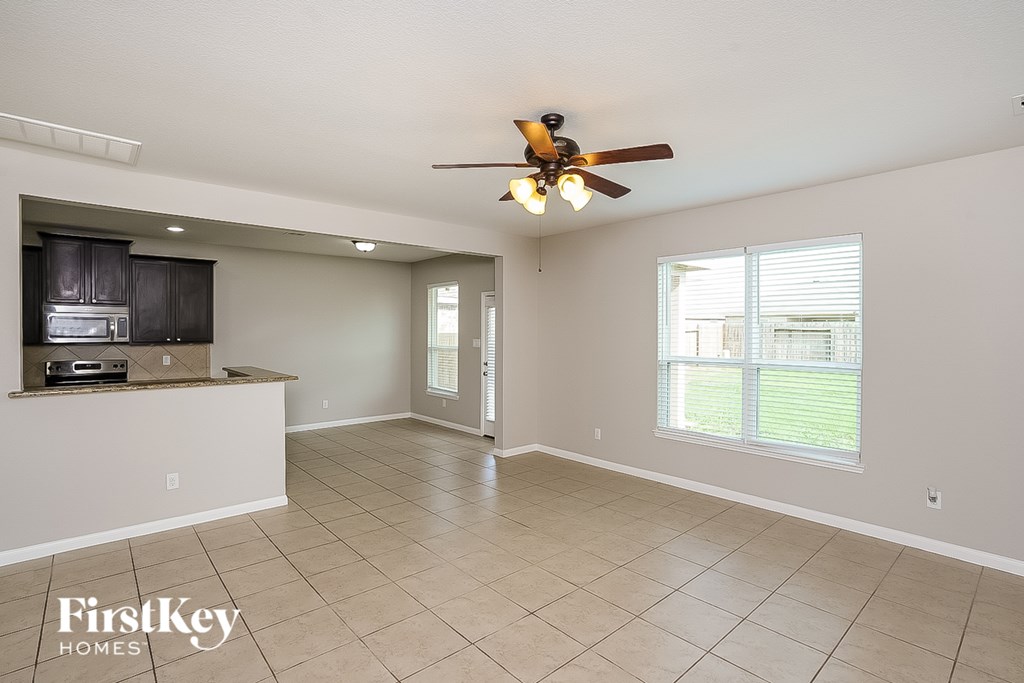 A spacious living room with a ceiling fan and a kitchen area in the background.