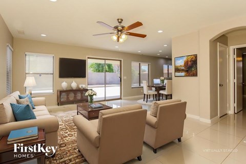 A living room with a fan, two chairs, and a table with a vase of flowers on it.