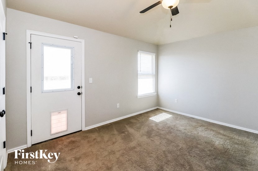 a living room with a carpet and a white door and a ceiling fan
