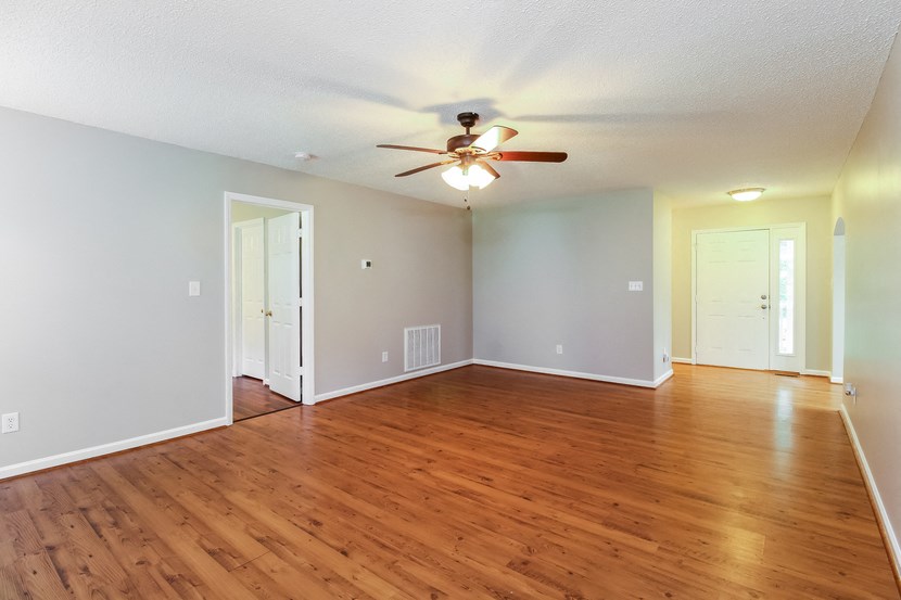 an empty living room with wood floors and a ceiling fan