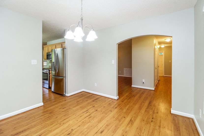 an empty living room with a hard wood floor and a stainless steel refrigerator