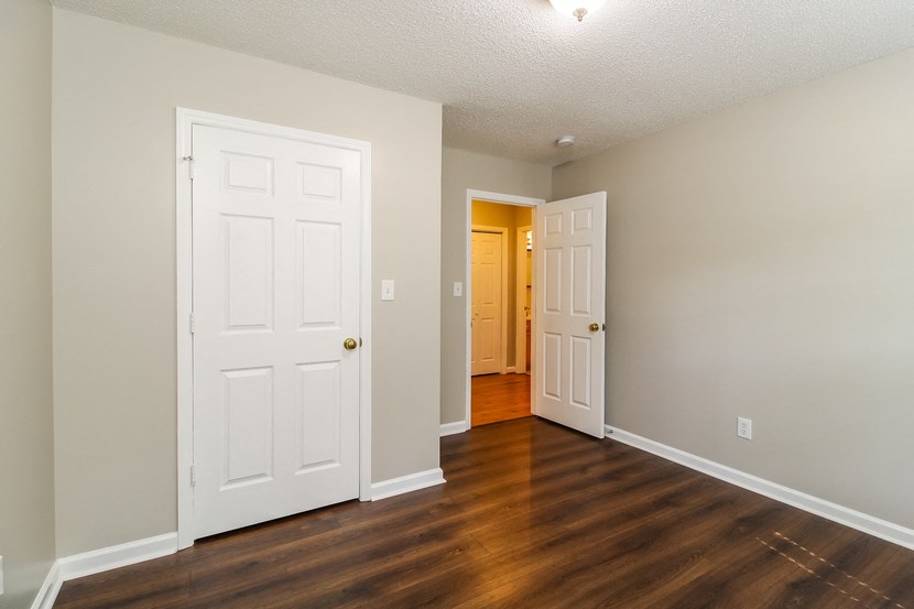 an empty living room with two doors and a hallway to a bedroom