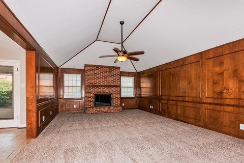 an empty living room with a brick fireplace and a ceiling fan