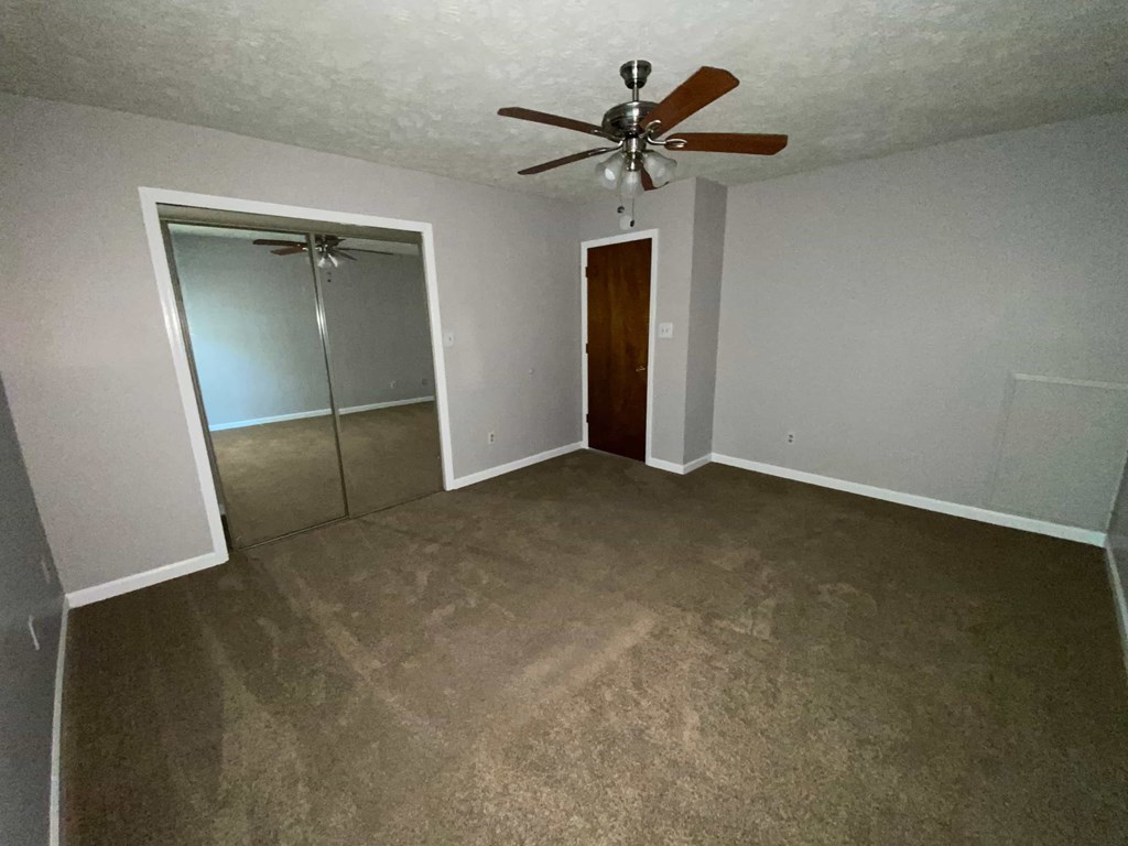 an empty living room with a ceiling fan and a closet