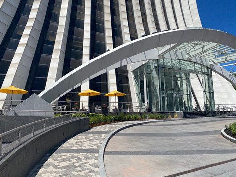 A modern building with a curved glass entrance and yellow umbrellas.