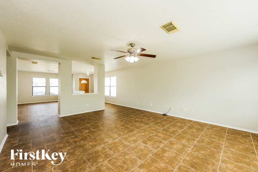 an empty living room with a ceiling fan and tile floors