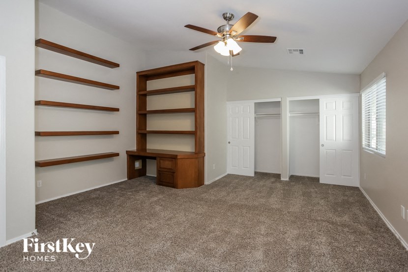 an empty living room with a ceiling fan and a book shelf