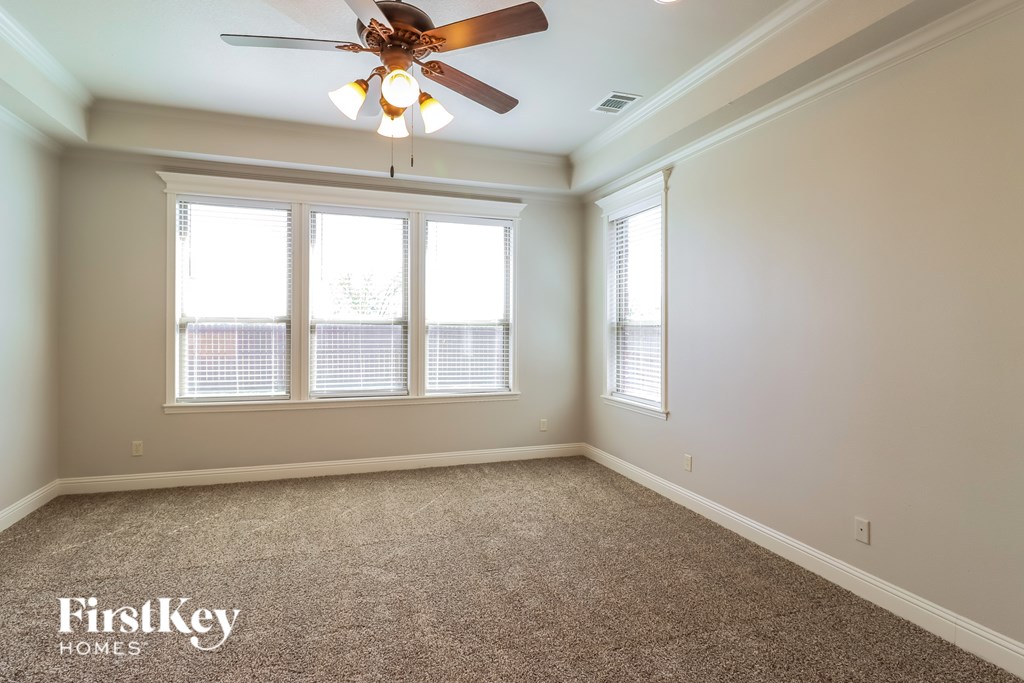 A room with a carpet floor, a ceiling fan, and two windows.