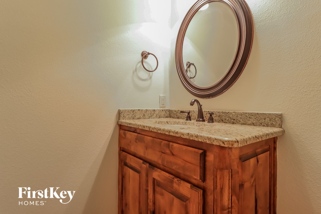 A bathroom sink with a round mirror and wooden cabinet.
