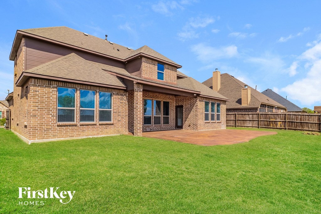 A brick house with a brown roof and a green lawn in front.