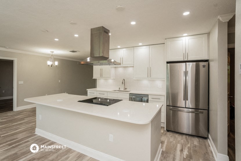 a white kitchen with a large island and stainless steel refrigerator