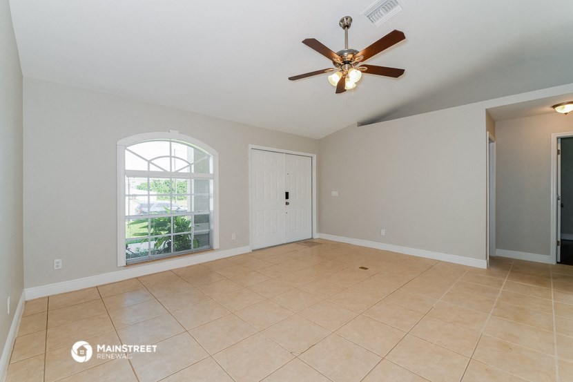 an empty living room with a large window and a ceiling fan