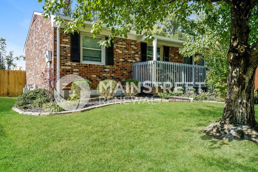 a small brick house with a porch and a tree in the yard