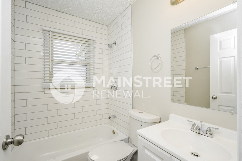 a renovated bathroom with white subway tiles and a white sink and toilet