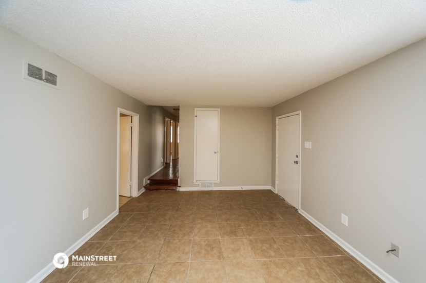 a spacious living room with beige tile and white walls