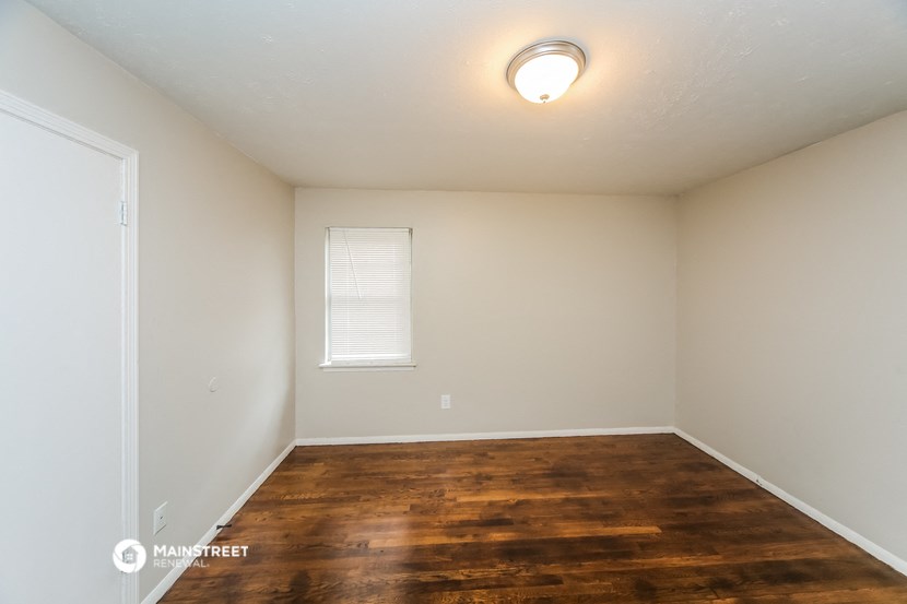 the spacious living room of an apartment with wood flooring and a window