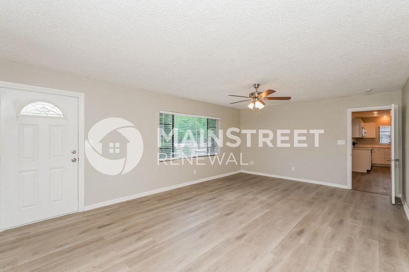 a spacious living room with a white door and a ceiling fan