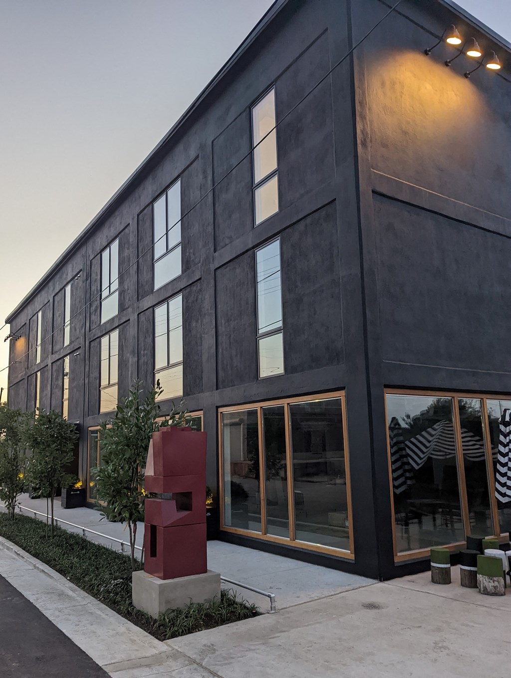 A modern building with a dark facade and a red sculpture in front.
