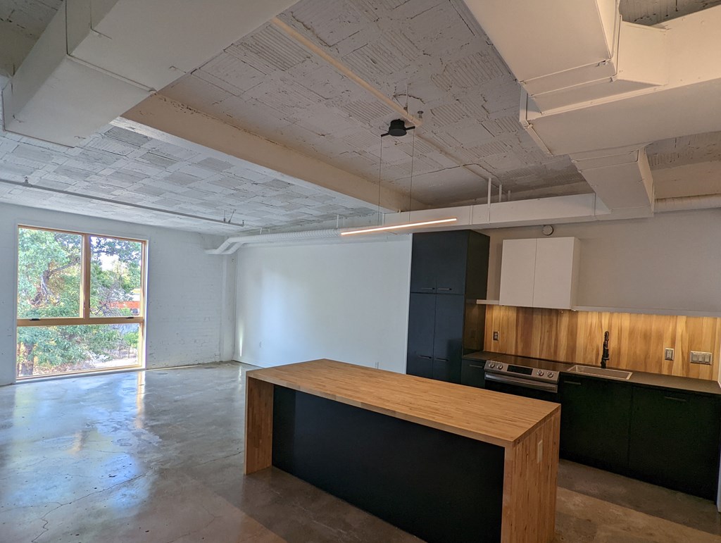 A room with a long wooden table and a kitchen area in the background.