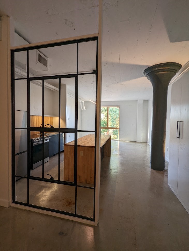 A black gate is open to a room with a white wall and a wooden box.