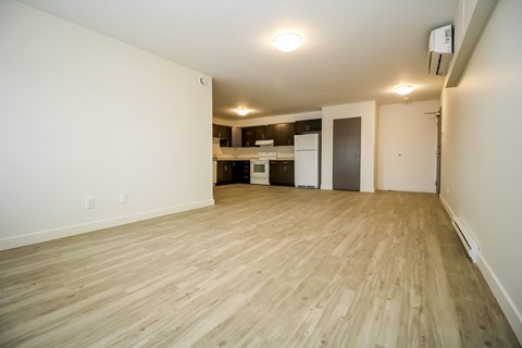 A room with wooden flooring and a kitchen area in the background.