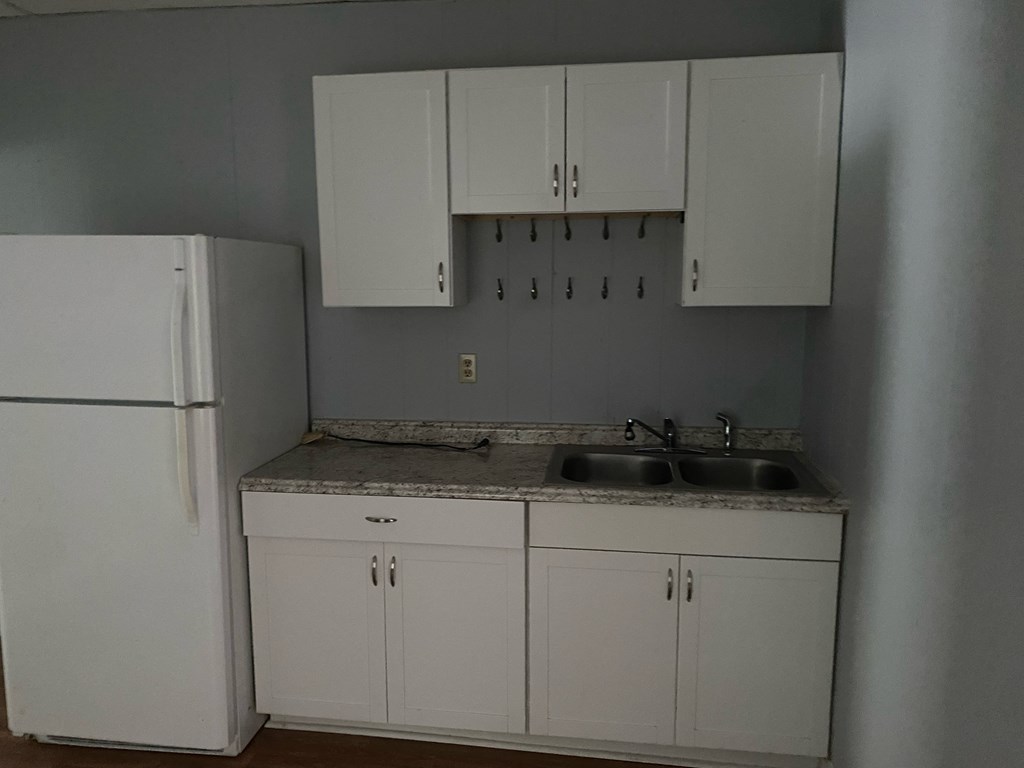 an empty kitchen with white cabinets and a refrigerator