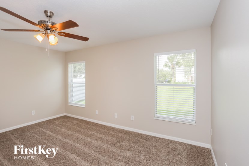 A room with a carpet floor, a ceiling fan, and two windows.