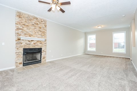 an empty living room with a fireplace and a ceiling fan