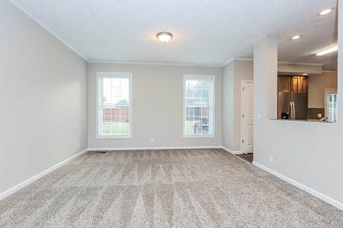 an empty living room with a kitchen and a window