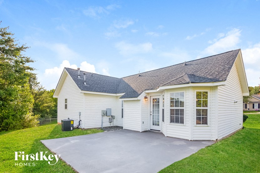 the backyard of a white house with a concrete driveway
