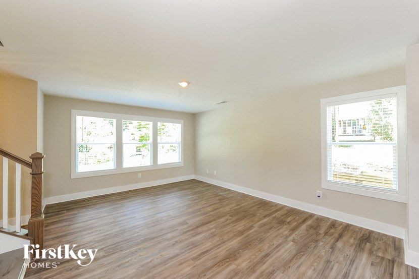 A room with wooden floors and two windows overlooking a tree-filled landscape.
