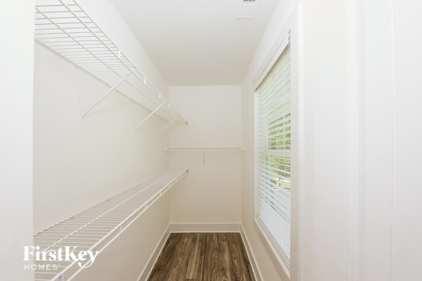 A white walk in closet with a window and wooden floors.