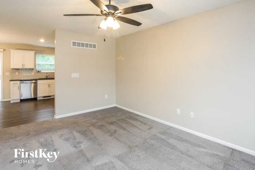 an empty living room with a ceiling fan and a kitchen